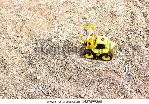 Toy loader on the beach. Excavator rowing sand.
Loader loads sand. Children's toys for sand. Yellow excavator toy
in the sand, on the beach. Summer holiday or summer vacation
concept. Turkey, Alanya.