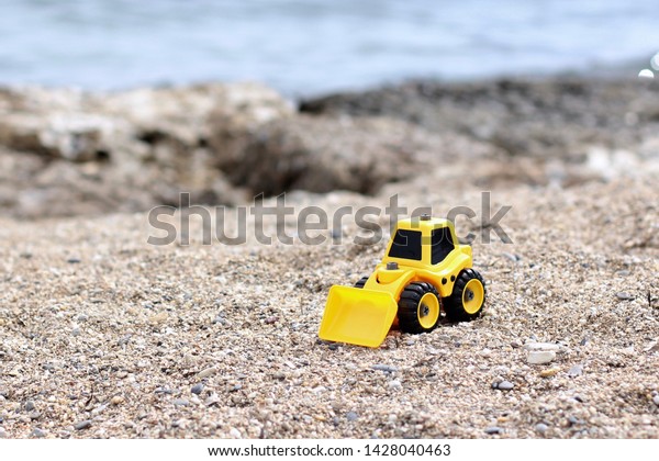 Toy loader on the beach. Excavator rowing sand.\
Loader loads sand. Children\'s toys for sand. Yellow excavator toy\
in the sand, on the beach. Summer holiday or summer vacation\
concept. Turkey, Alanya.