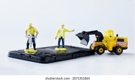 Toy Man Workers Repair Or Dispose Of An Old Mobile Phone Or Smartphone Using A Jackhammer And A Forklift Truck. Smartphone Repair Or Recycling Concept. Micro World. Close-up