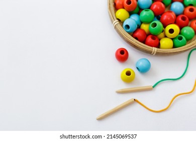 toy for motor skills development - colorful wooden beads, lace and needle over white background with copy space