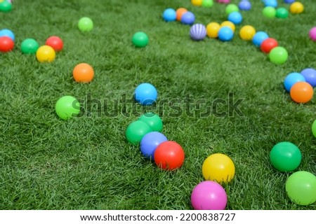 Toy multi-colored balls lie on the green grass. Plastic balls for children's games