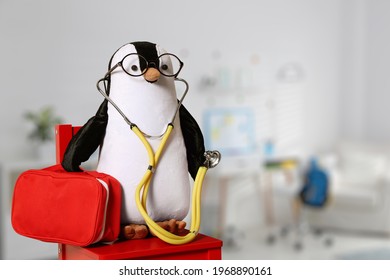 Toy penguin with eyeglasses, stethoscope and first aid bag indoors, space for text. Pediatrician practice