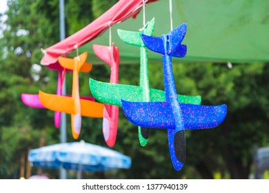 Toy Plastic Planes Of Different Colors. Children's Toy. Bright Planes Of Foam Hanging On The Large Outdoor Umbrella.