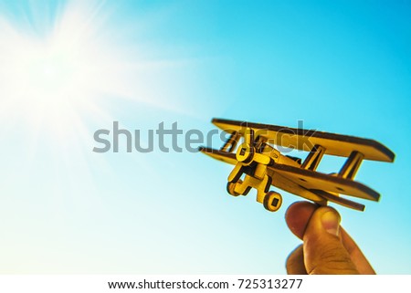 Toy of retro vintage airplane in man's hand against blue and yellow sky with clouds - a symbol of travel and dreams