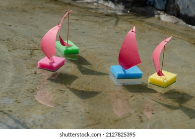 Toy Sailboats Made From Kitchen Sponges. Children's Sailing Regatta In The City Fountain. Four Children's Colorful Ships Are Floating In A Shallow Pond. Selective Focus. No People.