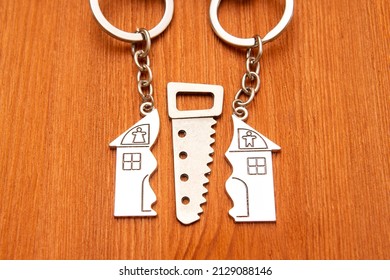 Toy Saw Between Two Split House Shaped Keychains On A Wooden Background. Splitting Property In A Divorce.