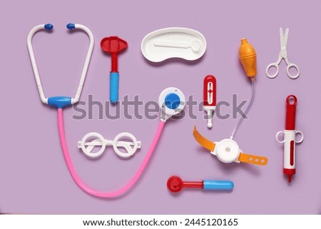 Toy stethoscope with thermometer and  reflex hammer on lilac background. Top view