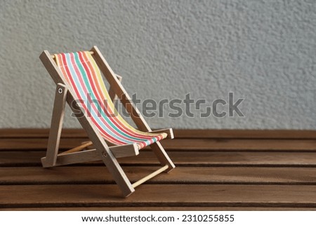 Toy sun lounger on table near light wall