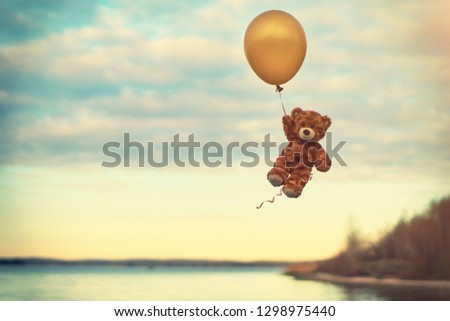  Toy teddy bear flying on a yellow balloon. Flight over the lake. Birthday.  Balloon.                              
