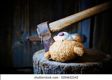 Toy teddy bear lying on a wooden log killed by an ax