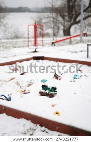 Toy tractor lying upside down in a snow-covered sandbox in an empty playground