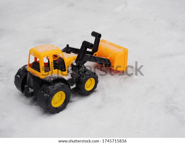 Toy tractor removes\
snow with a bucket in winter.\
A child\'s toy fights the snowfall by\
clearing the snow