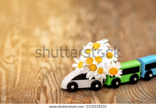 Toy train\
carries a bouquet of daisies . Wooden background with a bright\
texture.  Flower delivery.\
Concept