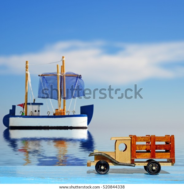 Toy truck car on a blue wooden surface and toy\
sailboat at sea