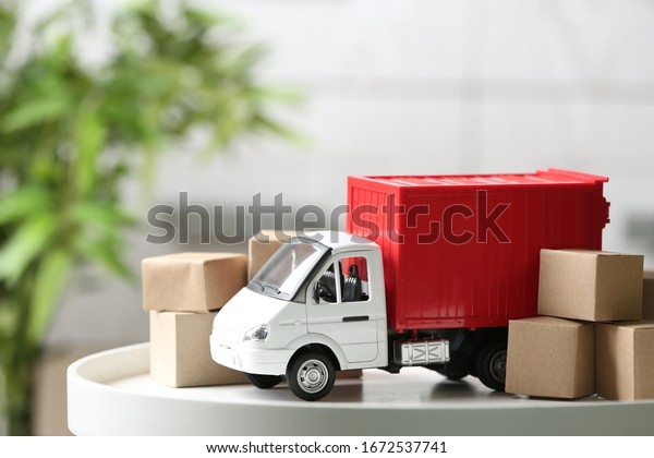 Toy truck and cardboard boxes on table\
against blurred background. Courier\
service