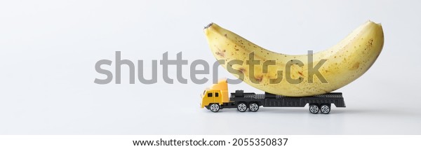 Toy truck carrying a fresh
yellow banana. White background. Delivery concept for oversized
items and fresh tropical fruits from the new harvest. Web banner.
Close-up
