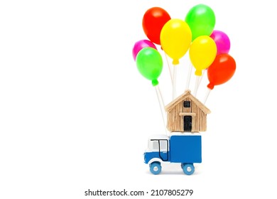 Toy truck with a miniature house model and a cluster of multicolored balloons isolated on white background. Fast moving service concept.