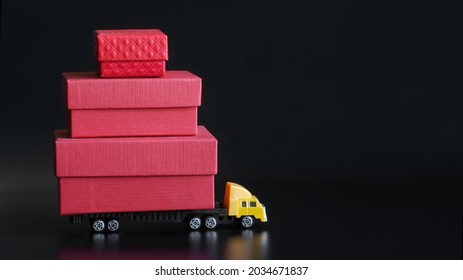 A toy truck transporting many red gift packing boxes against a black background. Black Friday sale and delivery concept. Free space for an inscription. Close-up