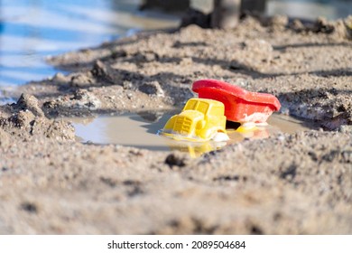 Toy Truck With Yellow Cab And Red Body In Puddle On Sand.