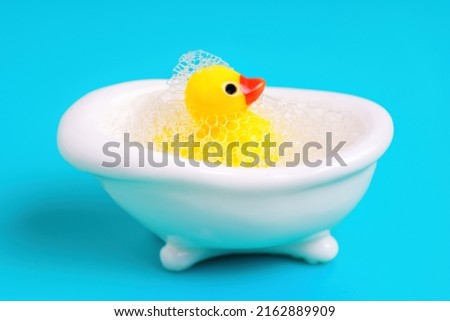 Toy yellow duck in a miniature white bathtub covered with soap bubbles. Bath time concept.