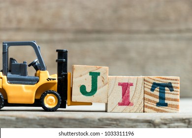 Toy yellow forklift hold letter block J to complete word JIT (Abbreviation of Just in time)on wood background