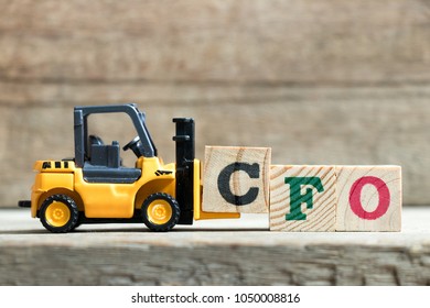 Toy yellow forklift hold letter block C to complete word CFO (Abbreviation of Chief Financial Officer) on wood background