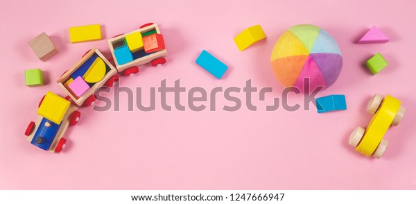 Toys background. Baby kids toys\
frame with toy cars, colorful wooden cubes on pink\
background