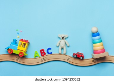 Toys background with copy space. Kids toys train, ABC letters, bear, car and pyramid on toy wooden railway on blue background with blank space for text. Top view, flat lay.