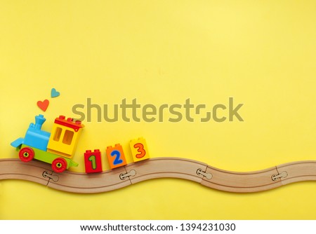 Toys background with copy space. Kids toy train with numbers on toy wooden railway on yellow background with blank space for text. Top view, flat lay.