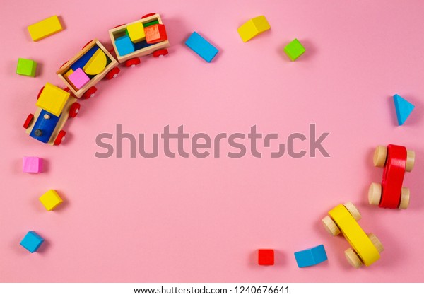 Toys background frame. Wooden toy train\
and cars with colorful blocks on pink\
background