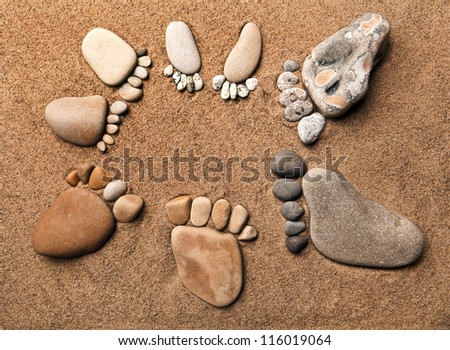 trace feet of a pebble stone on the sea sand backdrop , concept happy family