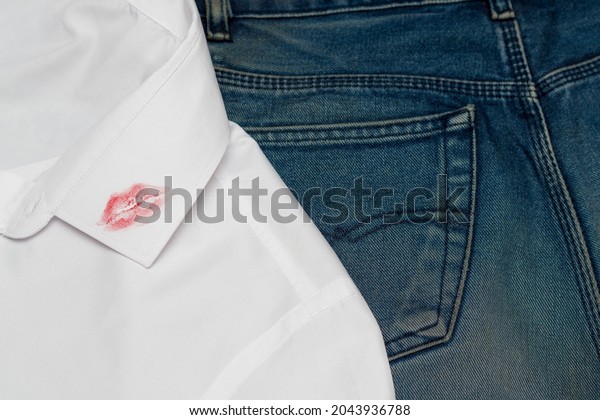 A\
trace of lipstick lips from a kiss on men\'s clothing. A white shirt\
is lying on blue jeans. The concept of\
infidelity.