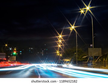 traces of car lights on the evening street. starburst of city lights. wide road leads to living area in the distance. busy night life concept