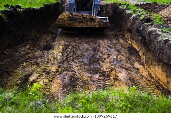 traces of excavator tires digging pit in grassy\
soil during earth works
