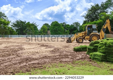 Track bulldozer, earth-moving equipment for land clearing, grading, ground excavation for new residential building with pile of fresh green glass patches for landscape. Lawn plant service, preparation