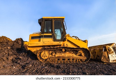 Track bulldozer, earth-moving equipment parking at construction site with bright blue sky background. Land clearing and grading machine for foundation of new building business. Machinery on the ground