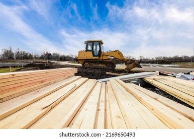 Track bulldozer, earth-moving equipment parking at construction site with pile of lumber planks and clouds blue sky background. Land clearing and grading machine for foundation of new building house.
