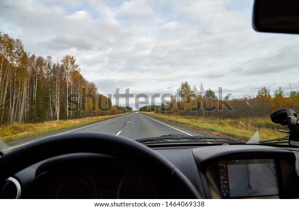 Track from the car window and white\
clouds on blue sky. Woman\'s hand on the steering wheel. Female\
driver seeing beautiful autumn landscape during travel in\
auto