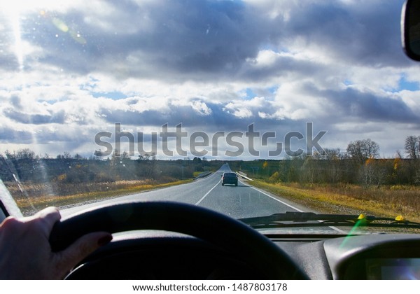 Track from the car\
window and white clouds on blue sky. Natural landscape during\
travel in auto. Woman\'s hand on the steering wheel. Female driver\
seeing beautiful\
landscape
