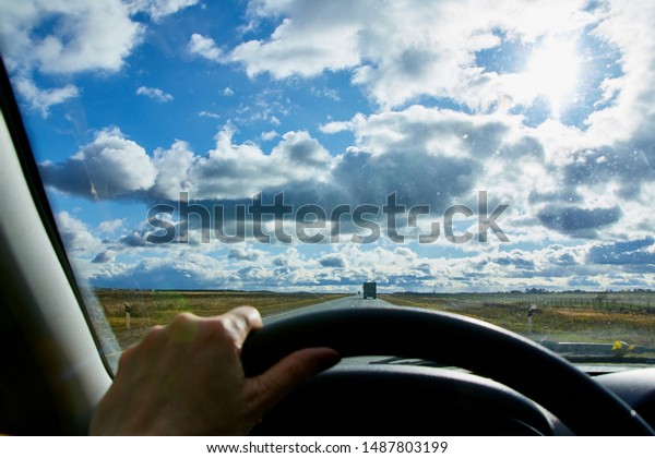 Track from the car\
window and white clouds on blue sky. Natural landscape during\
travel in auto. Woman\'s hand on the steering wheel. Female driver\
seeing beautiful\
landscape