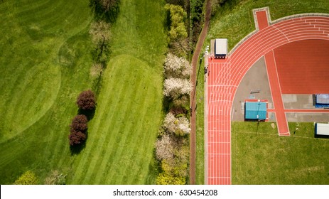 Track And Field. Abstract Aerial View Looking Down Onto A Professional Athletics Running Track Set Against The Green Of A Neighbouring Golf Course.