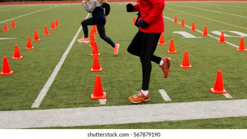 track teams sprinters perform drills over orange cones on a green turf field in the winter, - Powered by Shutterstock