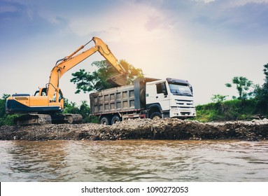 Tracked excavator loading soil and stone in a truck in the river. - Powered by Shutterstock