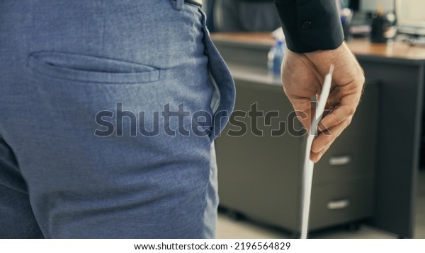 Tracking shot of office worker walking through\
the office to his workplace with documents in his hand. Close-up\
back side view of hand with\
documents