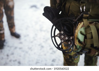 Traction Ice Cleats (anti-slip Microspikes) Hanging At The Waist Of A Man In Military Clothes. It Is An Accessory Designed To Be Attached To Shoes, Which Provides Extra Traction On Snow And Ice.