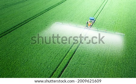 The tractor applies herbicides, pesticides or fertilizers to the green field.