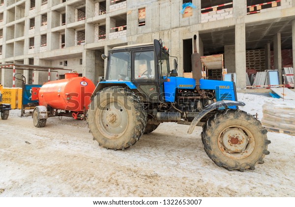 Tractor Belarus model 1221.2 with trailer tank with\
gasoline and diesel fuel at construction site of residential\
building. Sunny winter snowy evening day. Moscow city Russia\
February 2019.