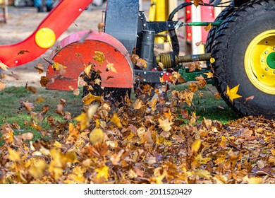 a tractor with a blower cleans a city park lawn and blows away autumn leaves, close-up view