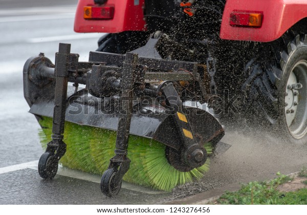 Tractor brush clean city sidewalks from\
dust and dirt. small car moving on road and clean asphalt with\
brushes and water. Cleaning of city by motor\
vehicles