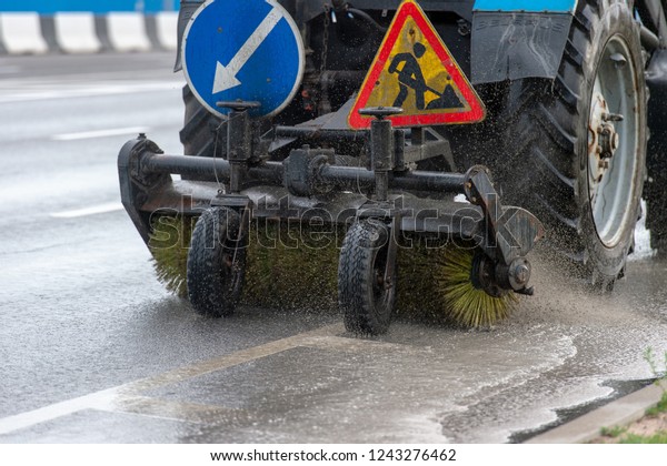 Tractor brush clean city\
sidewalks from dust and dirt. small car moving on road and clean\
asphalt with brushes and water. Cleaning city with car equipment\
rear view